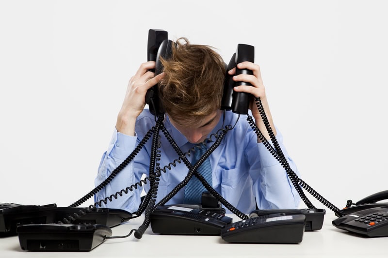 A man looking under pressure whilst managing too many phone calls.