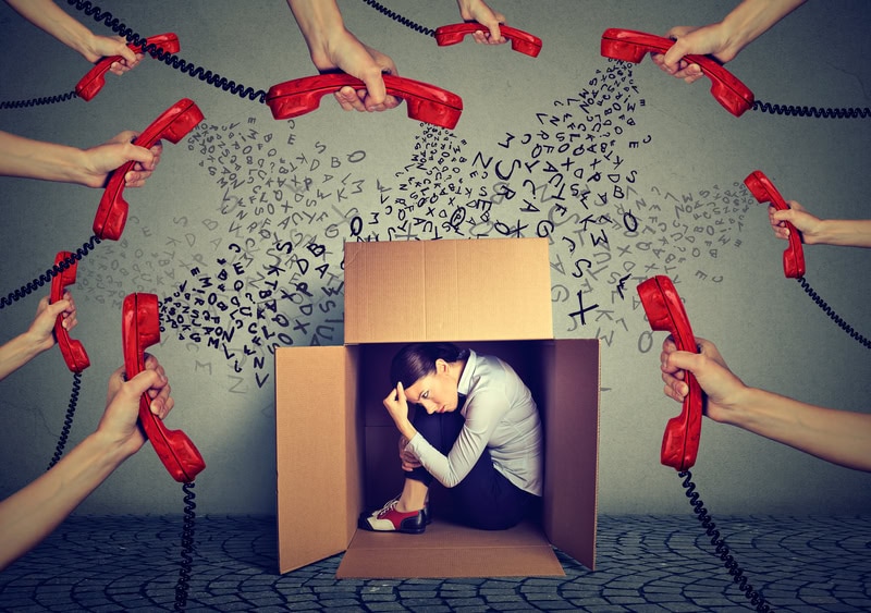 a woman hiding in a box from many armss holding red telephone receivers. the image represents stress